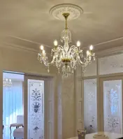 Křišťálový lustr s osmi rameny ve zlatém provedení zavěšený v luxusním interiéru s broušenými skleněnými dveřmi