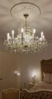 Křišťálový lustr Marie Terezie ve zlatém provedení zavěšený v luxusní ložnici s čalouněným nábytkem